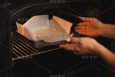 女人们的手放在烤箱里的一个烤盘和一个面糊蛋糕。