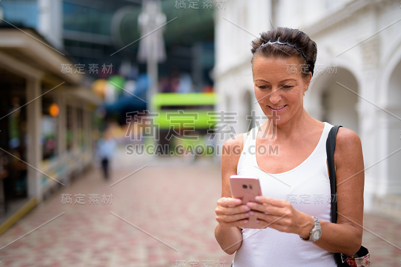 在新加坡翡翠山路上，一名成熟的女游客正在使用手机和短信