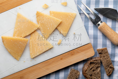 治愈羊奶酪。在白色大理石和面包上切成块。用叉子和刀吃奶酪。前视图。