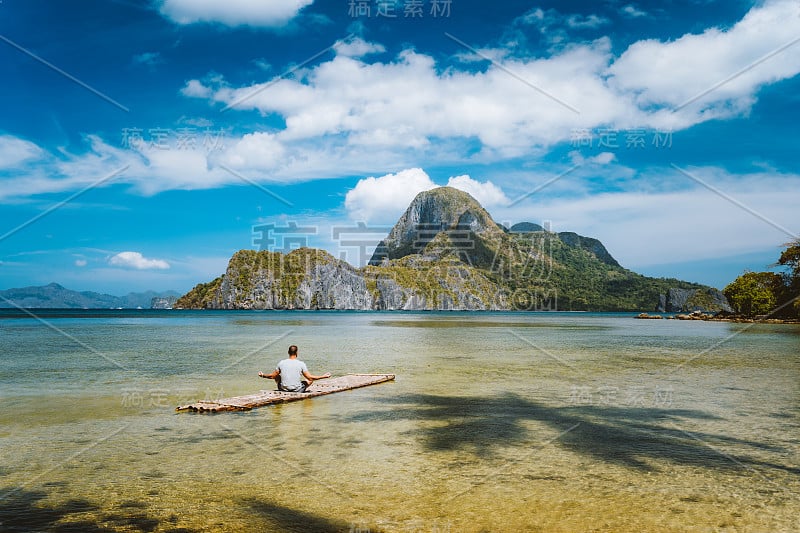 一个人在竹筏上沉思，周围是浅浅的泻湖水和远处的Cadlao湾的岛屿。菲律宾巴拉望省。节日假期的概念