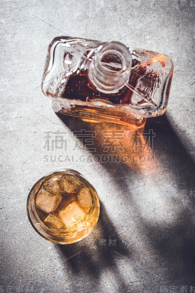 威士忌酒瓶和酒杯放在灰色的石头桌上。