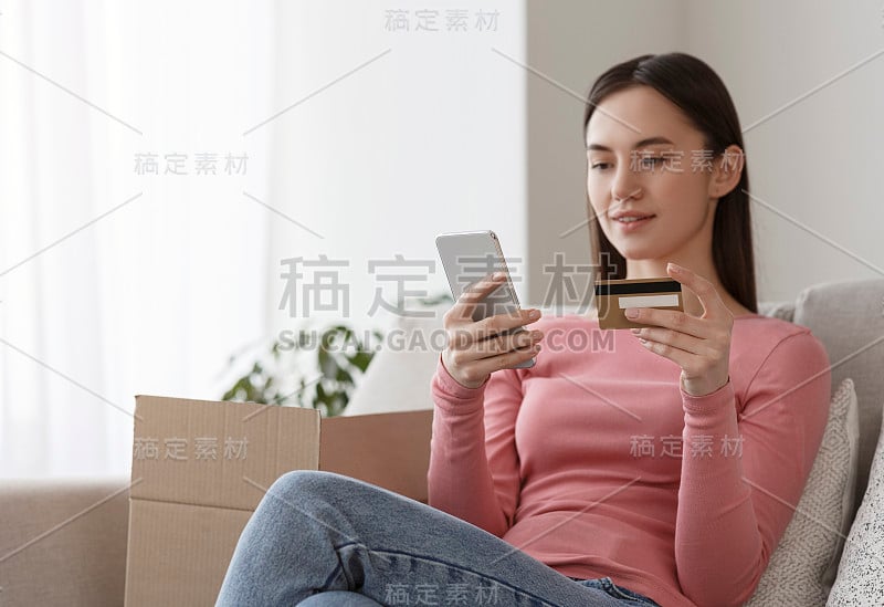 女人拿着信用卡，用手机输入信用卡信息