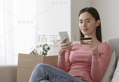 女人拿着信用卡，用手机输入信用卡信息