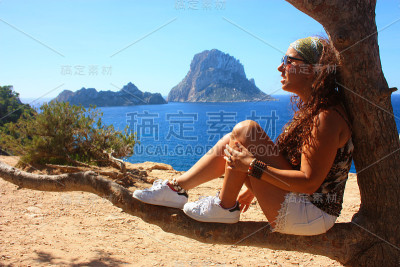 一个黑发白种女孩的暑假坐在树枝上欣赏埃斯韦德拉岛在卡拉霍特在伊比沙岛
