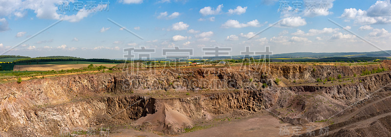 玄武岩(棕色岩石)采石场与岩石开采在夏季-蓝天与云，露天工厂和村庄和背景