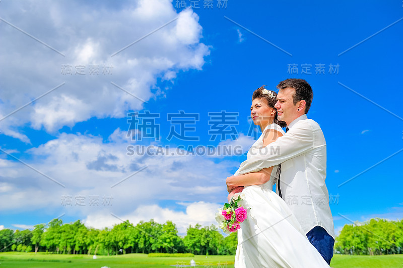 年轻英俊的新婚夫妇在公园散步:新郎拥抱新娘