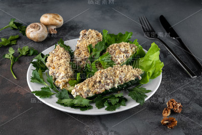 白色的盘子里塞满了黄瓜蘑菇和坚果沙拉，灰色的水泥背景和餐具，餐厅菜单的概念