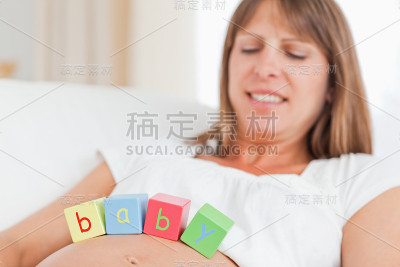 美丽的孕妇躺在沙发上玩积木