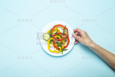 一位女士的手拿着一个蓝色背景上放着切碎的蔬菜的盘子。俯视图，平放