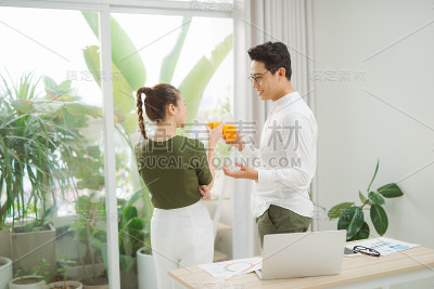 可爱的微笑夫妻在阳光明媚的日子里一边工作一边喝橙汁