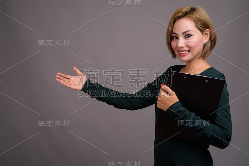 工作室拍摄的美丽的亚洲女人短发穿着长袖绿色连衣裙，以灰色的背景