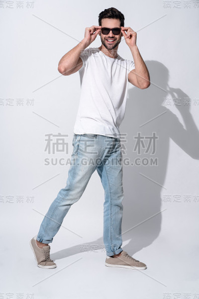 全长英俊的年轻人在眼镜和休闲装看着镜头和微笑，而站在白色的背景