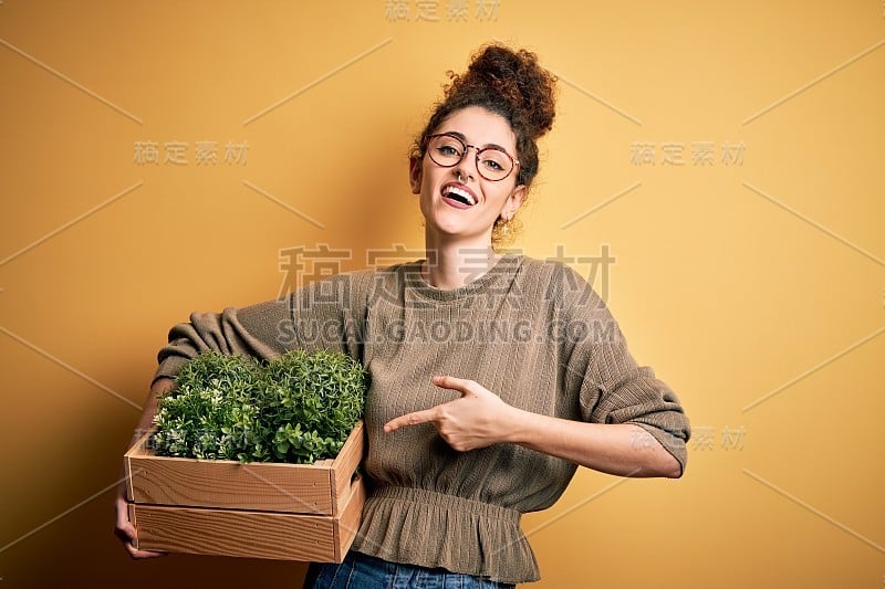 年轻美丽的园丁女人与卷头发和刺拿着木盒子与植物非常幸福的手指和手