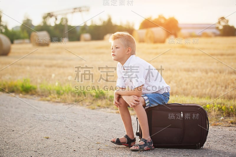 在夏日阳光明媚的日子里，孩子坐在手提箱上，