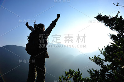 欢呼的女徒步旅行者在山顶张开双臂