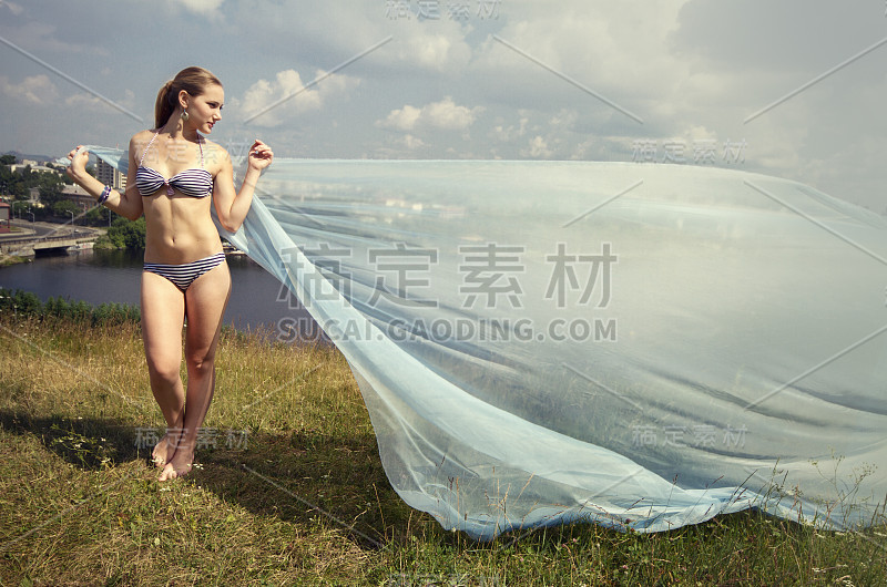 美丽迷人和性感性感年轻的成年漂亮的金发女人在夏天的阳光下穿着比基尼泳装与蓝色网格布