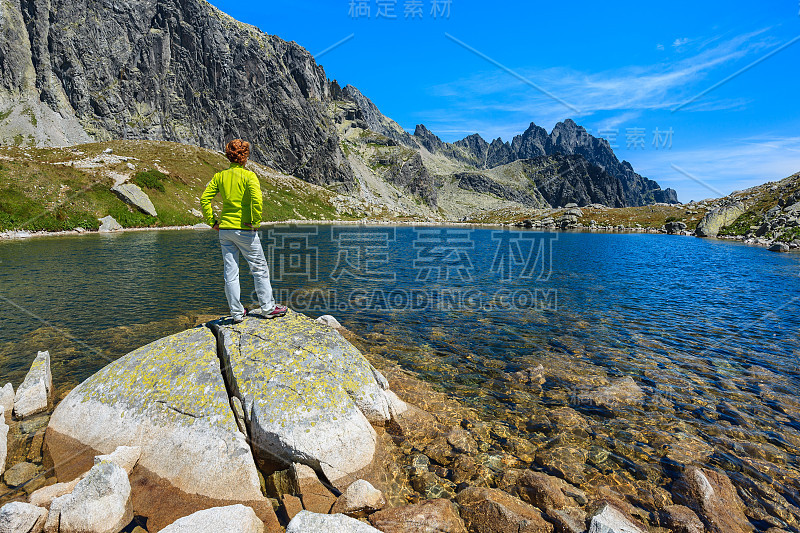 年轻女子游客站在一个岩石上的高山湖在夏季景观的斯塔列斯纳山谷，高塔特拉山