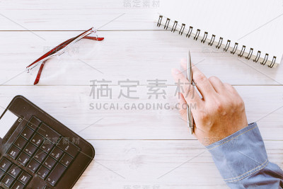 手拿着笔放在木桌上，桌上放着办公用品