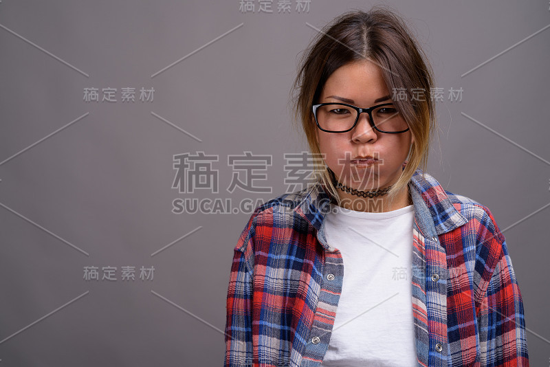 工作室拍摄的年轻亚洲妇女穿着格子衬衫，以灰色背景