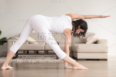 年轻迷人的女子在乌特西塔三角式姿势，客厅