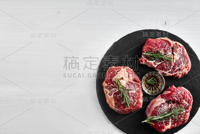 新鲜的生牛排配香草，大蒜，橄榄油，胡椒，盐和迷迭香在黑板上:里脊肉，Striploin，肋眼