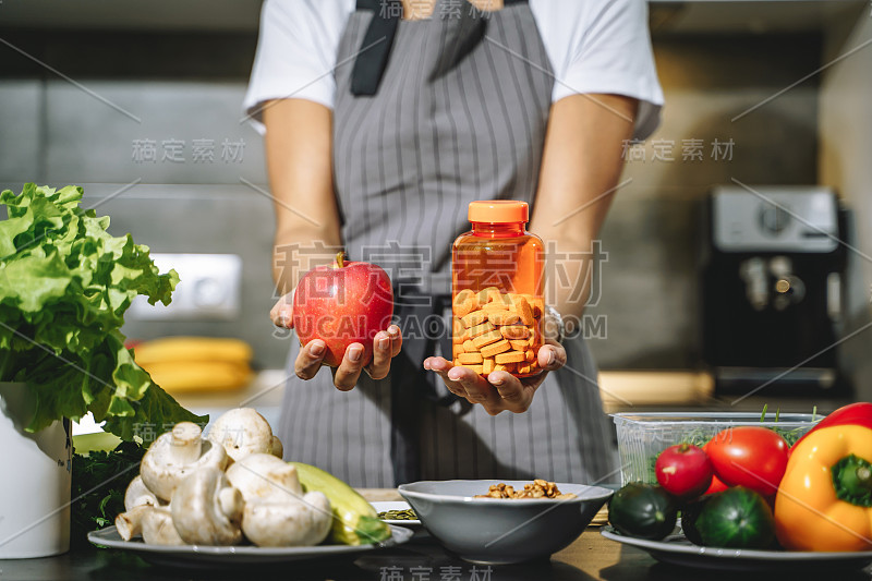 近距离的女性手拿着苹果和营养补充剂或维生素在厨房。选择、均衡饮食和健康理念