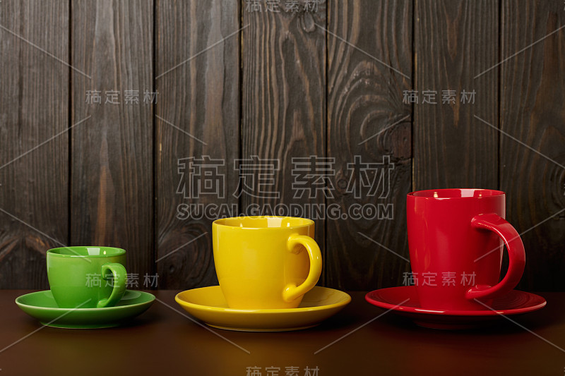 不同大小和颜色的陶瓷杯咖啡和茶-红色，黄色和绿色在黑暗的木制背景。