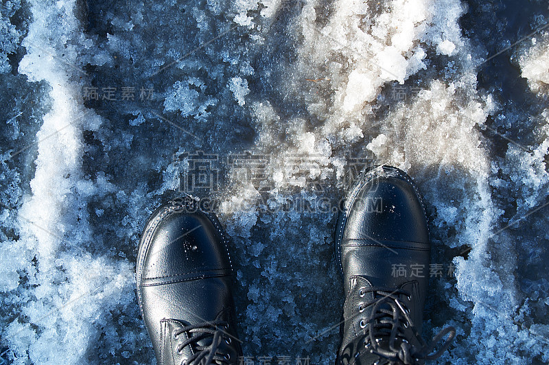 在潮湿的天气穿着黑色靴子的脚。融化的雪。从以上观点。