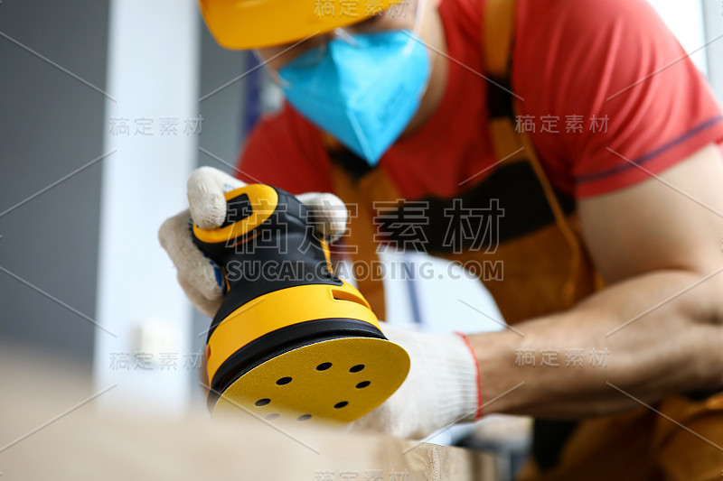 男建筑工人戴安全帽和防护面罩，使用打磨机