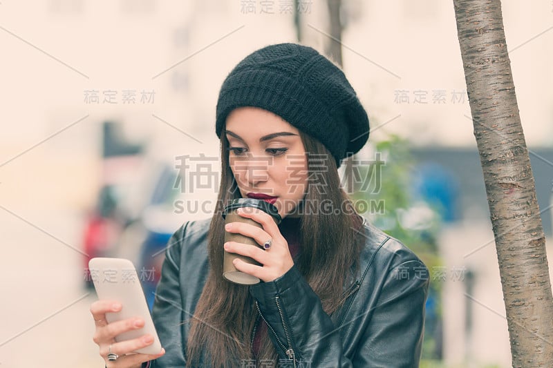 一个在户外拿着手机喝着咖啡的都市女孩。