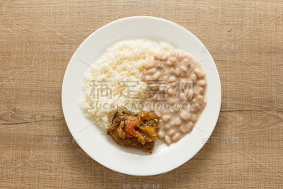 白米饭，花豆和肉酱。木桌上的白色盘子。头顶上，平摊的午餐。