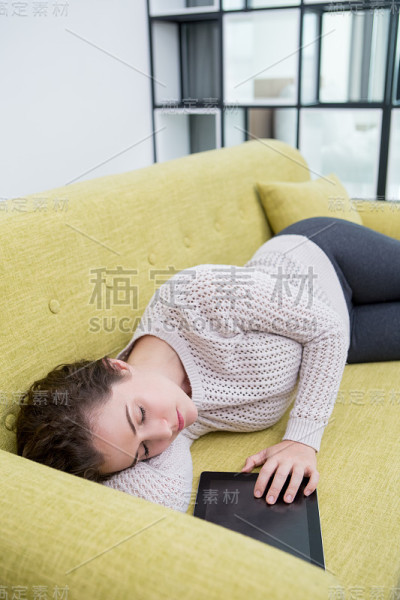 冷静的年轻女子在沙发上用平板电脑打瞌睡