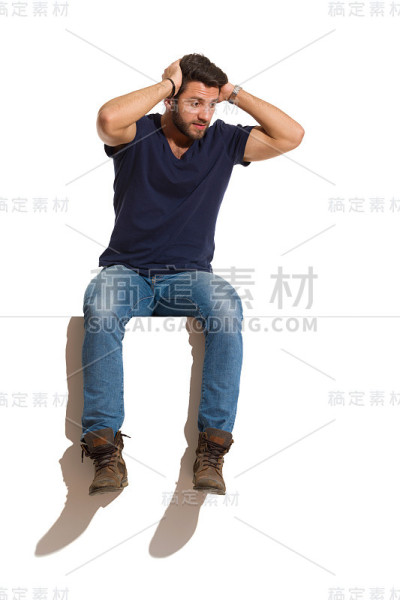 一个焦虑的英俊男子坐在山顶上，双手抱头向下看