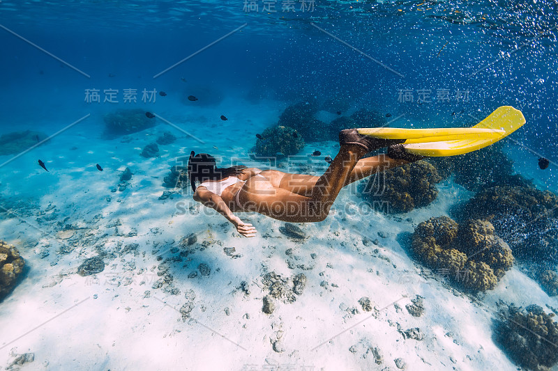 女人用黄色的鳍在沙滩和珊瑚上滑翔水下。