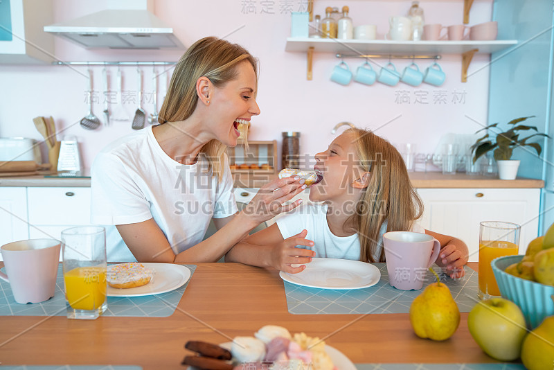 妈妈和女儿正在厨房里吃甜甜圈。可爱的家庭照片。穿着白色t恤