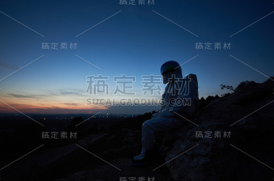日落时宇航员坐在岩石山上。