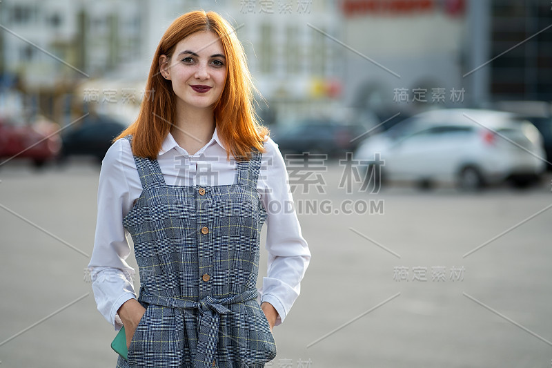 一个微笑的十几岁的女孩的肖像红头发和清澈的眼睛穿着时尚的休闲服装站在外面在温暖的夏天。