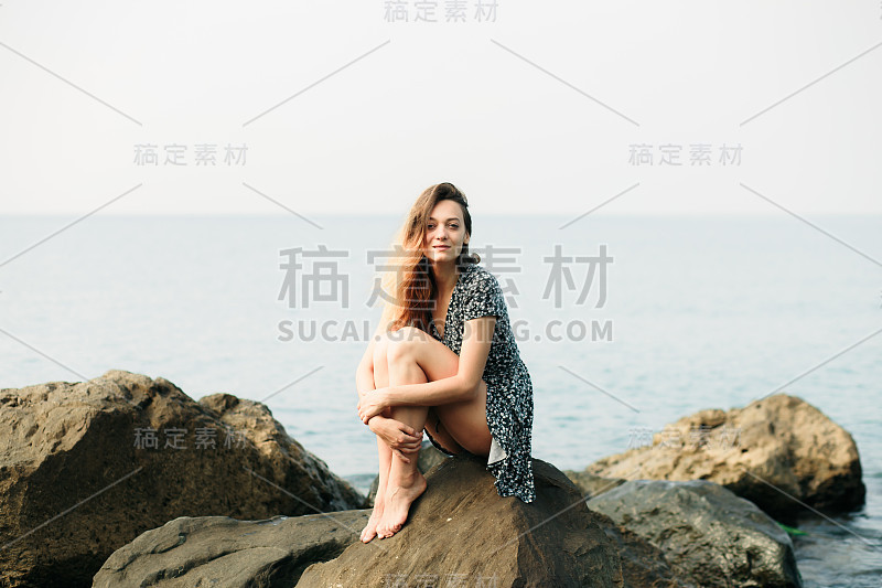 一个年轻美丽的女孩穿着大石头，风景如画的海边