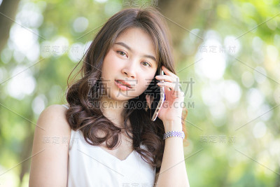 迷人的亚洲美女坐在绿色草地上谈论智能手机