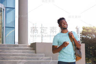 拿着包和手机走在楼梯上的男大学生