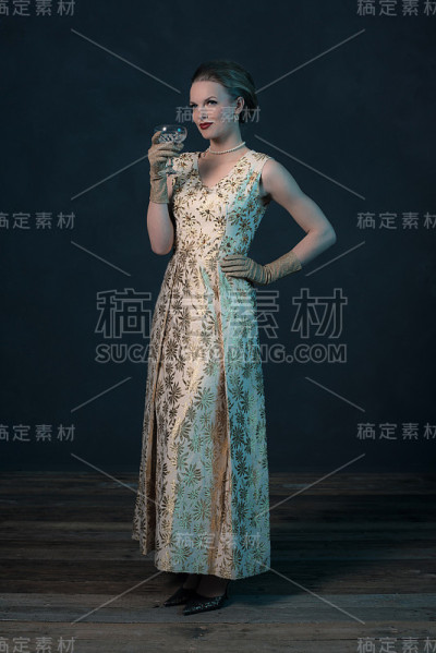 别致的复古50年代的时尚女人在金色的裙子拿着玻璃。