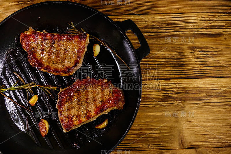 烤猪肉排与迷迭香，大蒜和香料在铸铁烤锅在木桌上。俯视图