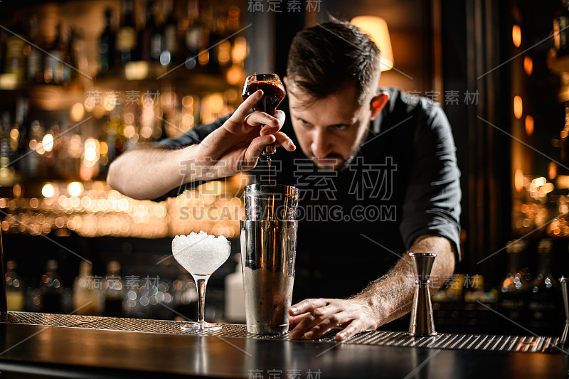 调酒师将深棕色的苦酒从玻璃瓶倒入钢质摇酒器