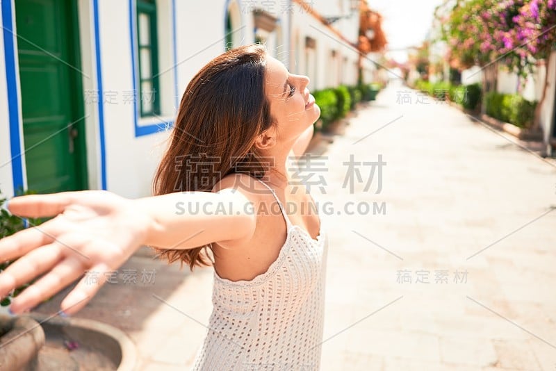 年轻美丽的女人在波多莫根村，快乐地微笑着，张开双臂在夏天的街道上晒太阳