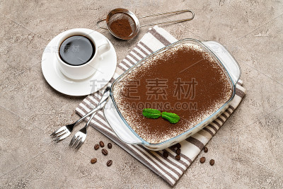 传统的意大利提拉米苏甜点在玻璃烤盘和一杯新鲜的热咖啡在混凝土背景