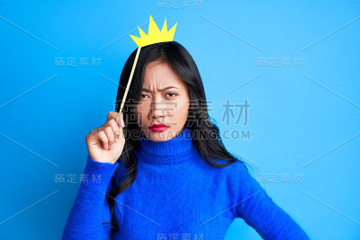 愤怒的年轻女子与纸皇冠粘在蓝色的背景。