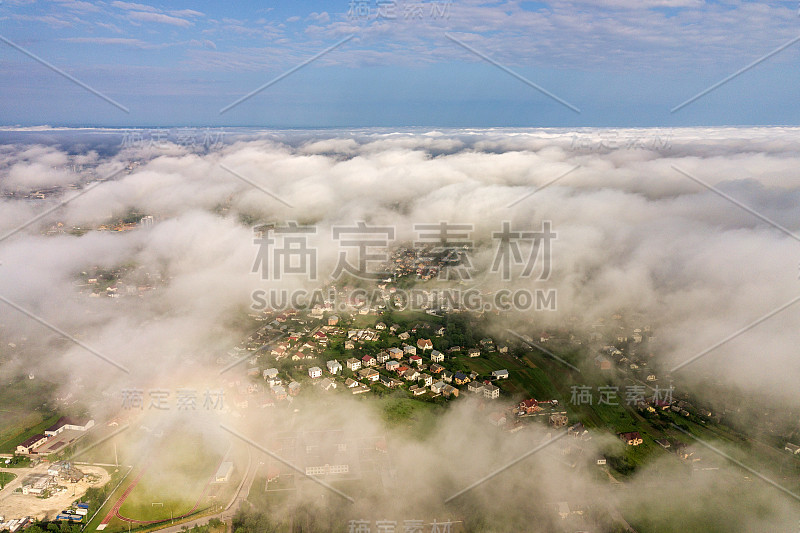 从空中俯瞰一个城镇或村庄，在夏天的绿色田野之间有一排排的建筑物和弯曲的街道。从上面俯瞰乡村景观。