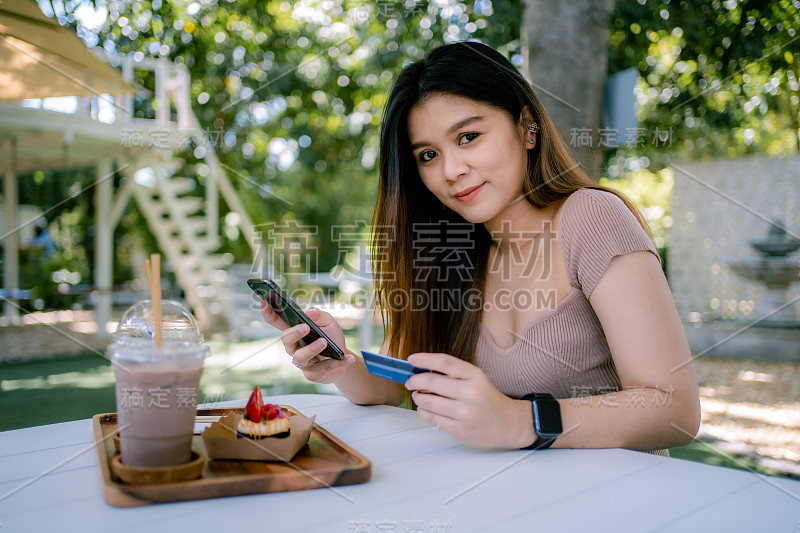 美丽微笑的年轻亚洲女性管理网上银行与手机应用程序在智能手机上，并进行移动支付与信用卡。