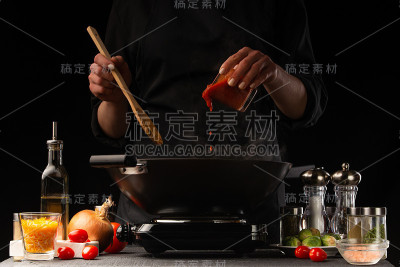 厨师将蕃茄酱与肉和蔬菜一起放入锅中。冻结。餐厅菜单,烹饪。在黑色背景上，图片用于广告或设计，餐厅经营