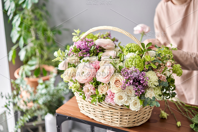 花店概念。花匠在柳条篮子里制作插花。一束美丽的混合鲜花。英俊的新鲜一些。花交付。